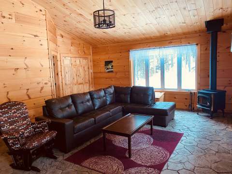 The chalet living room features a comfortable sofa, a chair, and a wood stove.
