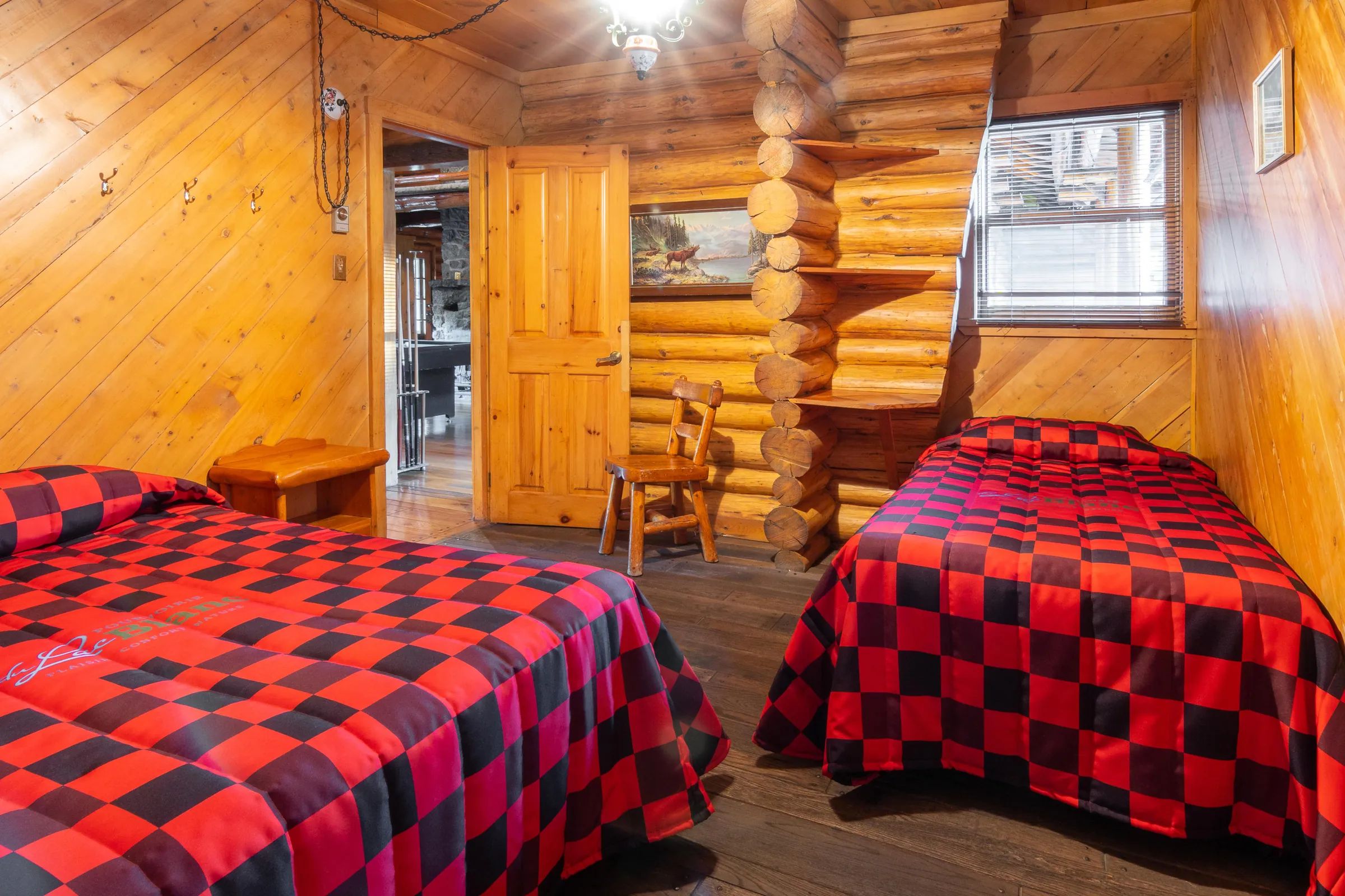 This rustic bedroom is equipped with two beds featuring red and black plaid bedspreads.
