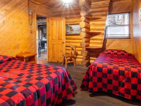 This rustic bedroom is equipped with two beds featuring red and black plaid bedspreads.