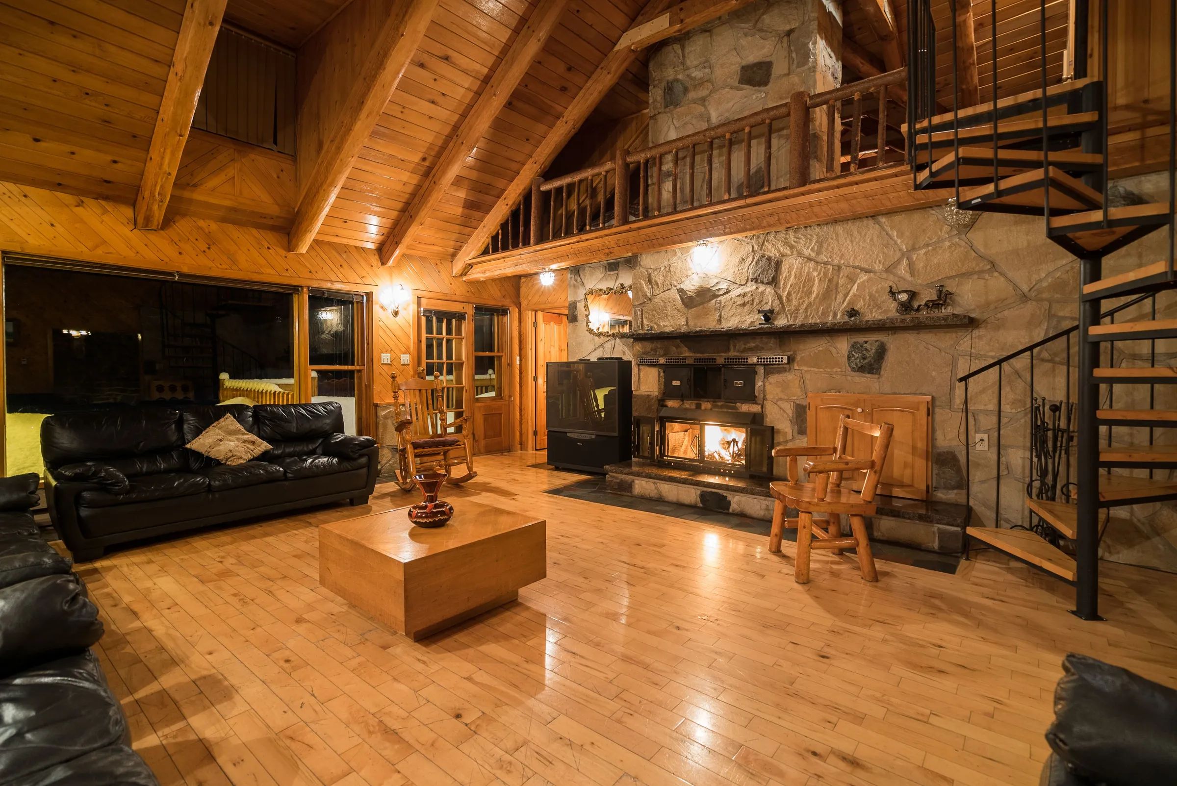 The chalet's cozy living room features a stone fireplace and a spiral staircase.