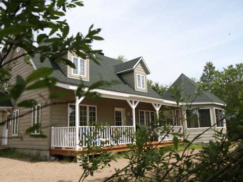 Side view of a large wooden cottage featuring a covered porch and numerous windows.