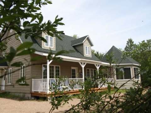 Exterior view of the spacious cottage surrounded by trees with its large porch.