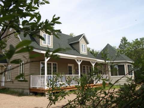 Exterior view of a large cottage with a covered deck surrounded by the forest.