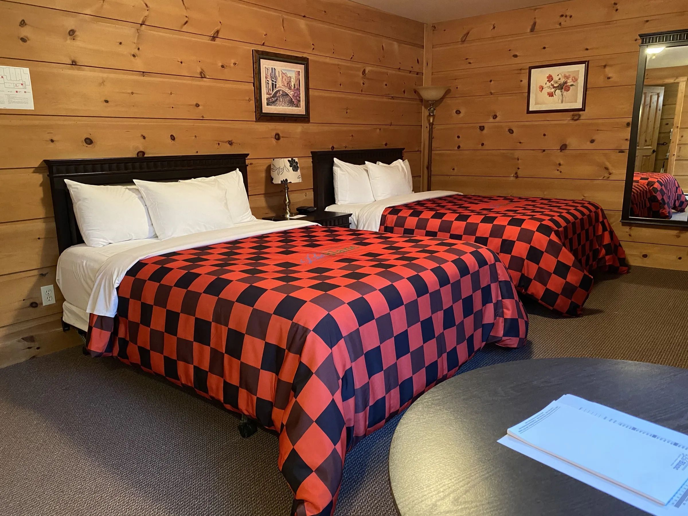 This rustic room features two double beds with red and black checkered bedspreads.
