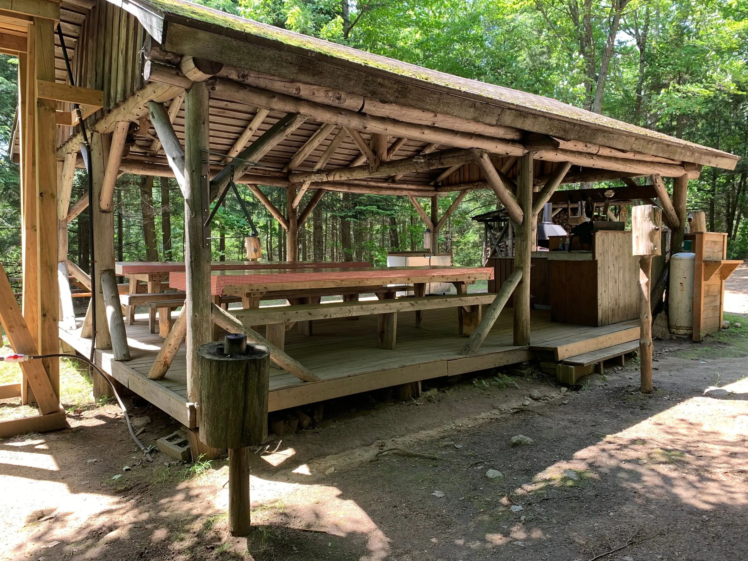 Cette structure en bois couverte abrite une grande table de pique-nique et un espace de cuisine.