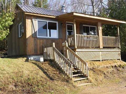 Front facade and porch of cabin number 6 located in the woods.