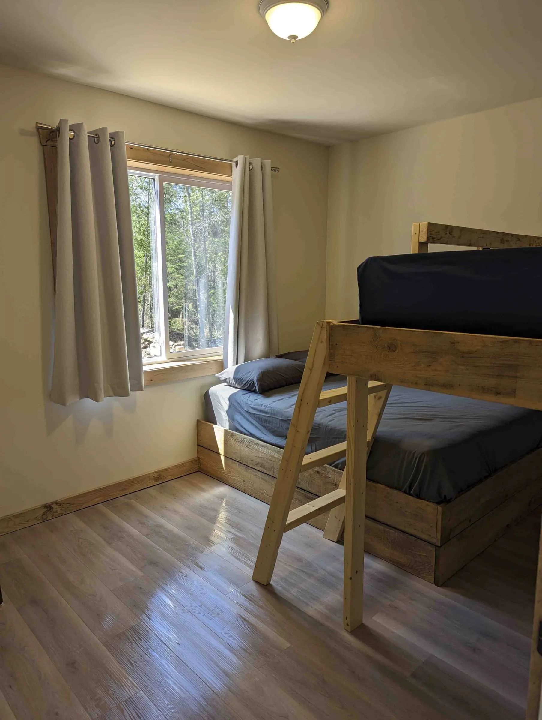 This cabin bedroom features a wooden bunk bed and a window overlooking the forest.