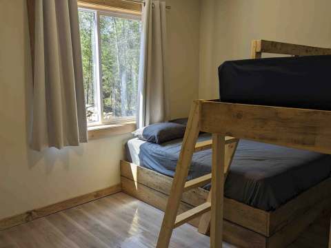 This cabin bedroom features a wooden bunk bed and a window overlooking the forest.