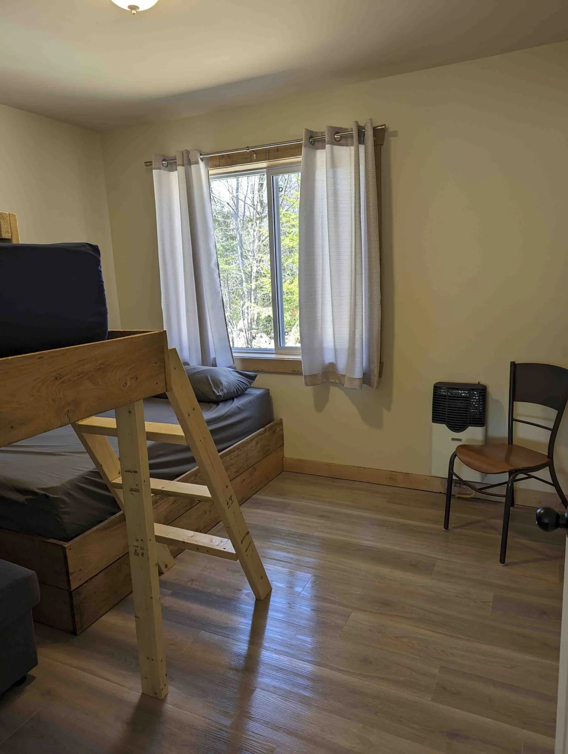 This cabin bedroom features a wooden bunk bed and a window overlooking the forest.