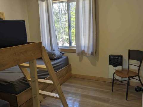 This cabin bedroom features a wooden bunk bed and a window overlooking the forest.