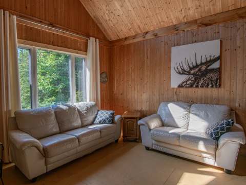 Le salon du chalet de l'Orignal propose deux canapés confortables dans une ambiance chaleureuse en bois.