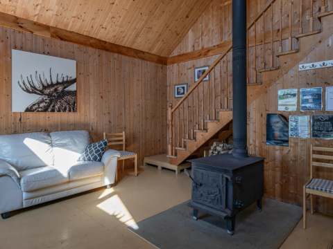 L'aire de vie principale du chalet comprend un poêle à bois, un canapé et un escalier en bois.