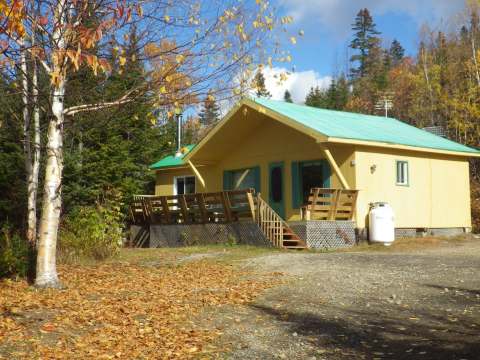 Le Chalet du Trappeur avec sa galerie en bois et son toit vert en automne.