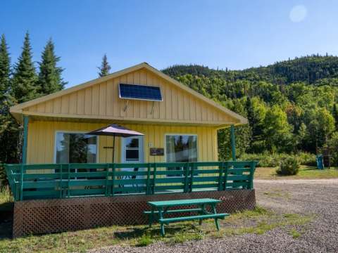 Le chalet jaune avec sa galerie verte et sa table de pique-nique offre un accès direct à la nature.