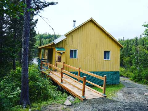 Vue latérale du Chalet du Bûcheron avec sa passerelle d'accès en bois en forêt.