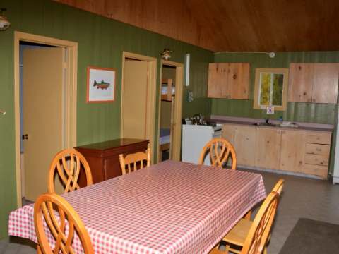 Vue d'ensemble de la cuisine et de la salle à manger du chalet, incluant une table et des lits.