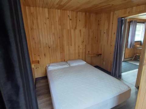 Cette chambre rustique est aménagée avec un lit double et des murs en lambris de bois.