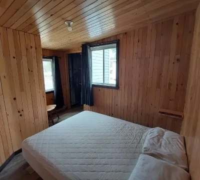 Cette chambre comporte un lit double dans un décor tout en bois avec deux fenêtres.