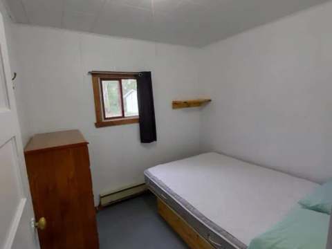 Cette chambre à coucher simple dispose d'un lit avec draps et d'une commode en bois.