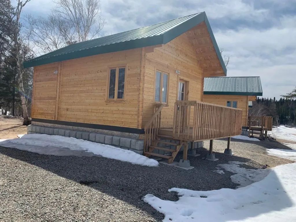 Side view of the wooden cabins with deck and metal roof, surrounded by residual snow.