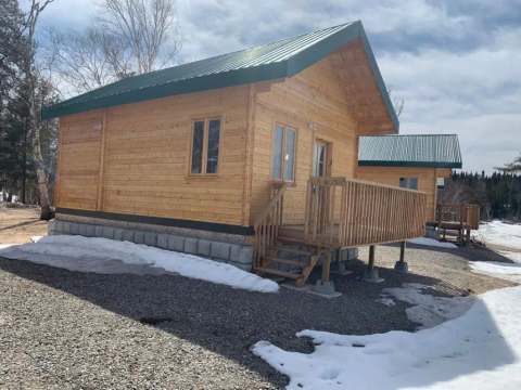 Side view of the wooden cabins with deck and metal roof, surrounded by residual snow.
