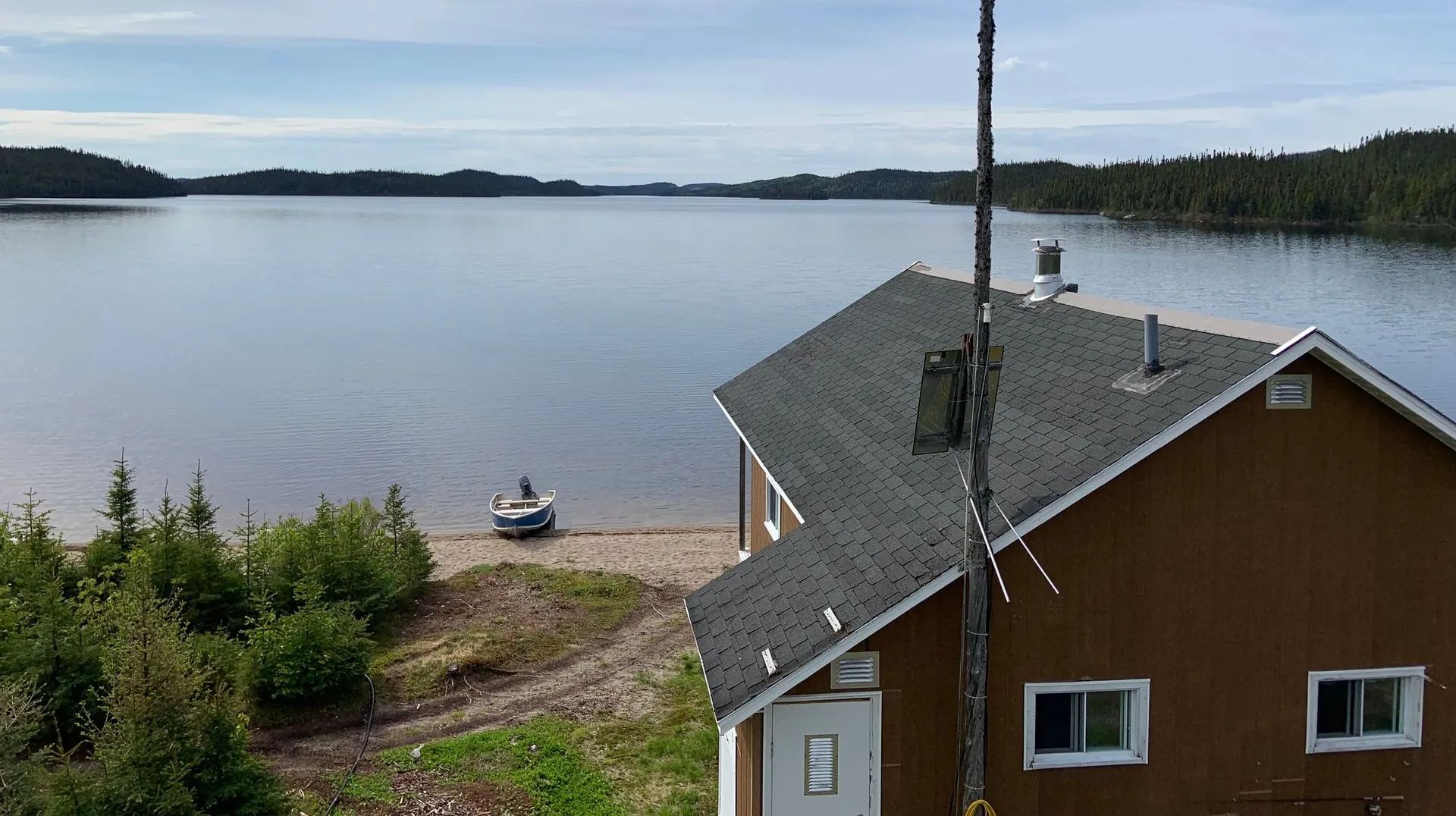 Vue aérienne du chalet Pimbina situé au bord du lac avec une embarcation sur la plage.