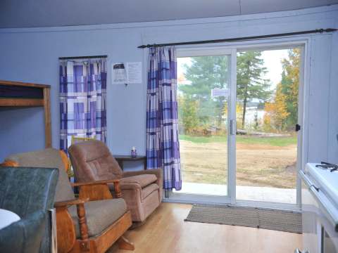 Vue de l'intérieur du chalet avec ses fauteuils, ses lits superposés et sa grande porte-patio.