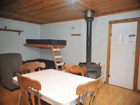 This room includes a dining table, bunk beds, and a wood stove.