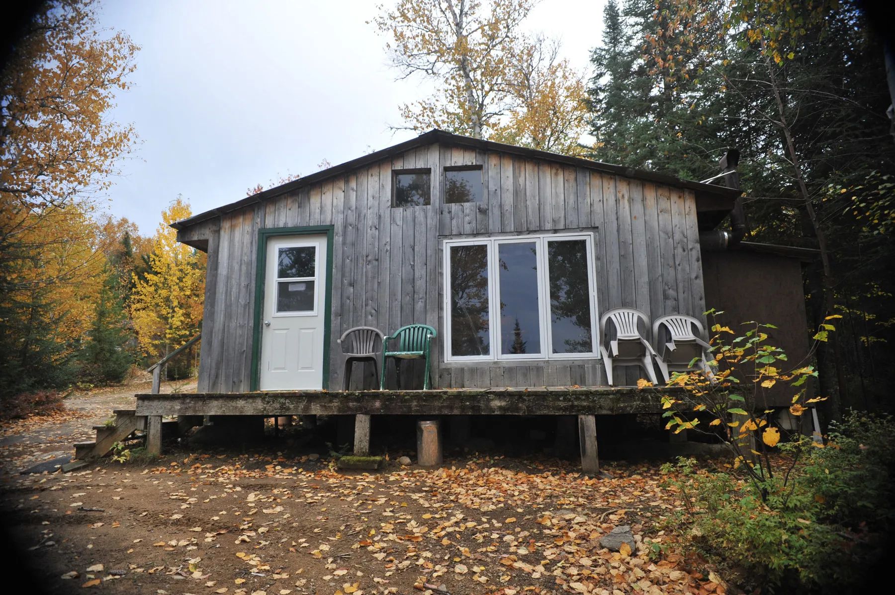 Vue extérieure du chalet Rustique avec sa galerie et ses chaises en forêt à l'automne.