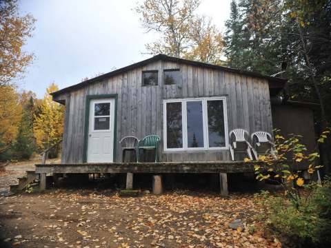 Vue extérieure du chalet Rustique avec sa galerie et ses chaises en forêt à l'automne.