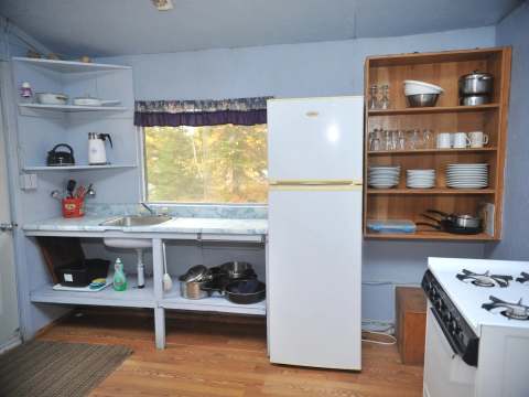 La cuisine fonctionnelle du chalet Le Rustique comprend un réfrigérateur, une cuisinière et la vaisselle.