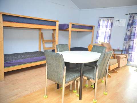 La salle commune du chalet comprend des lits superposés en bois, une table à manger et un coin salon.