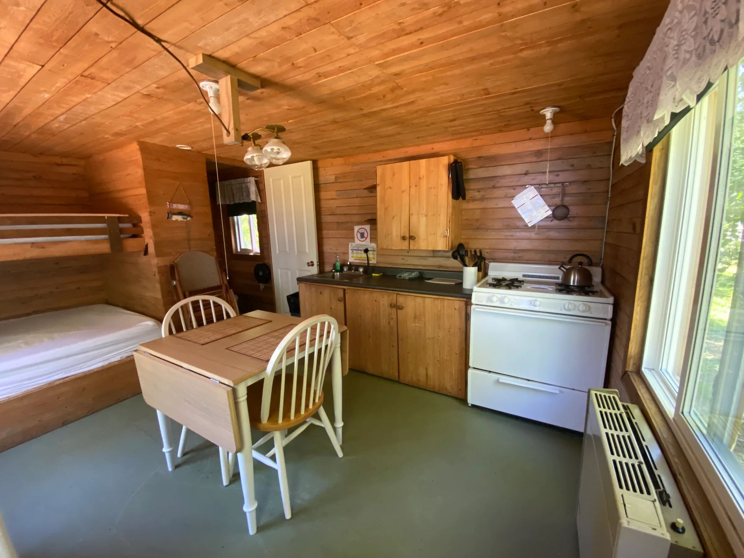 Vue de l'intérieur du chalet comprenant un coin cuisine, une table à manger et un lit superposé.