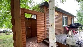 Un chalet en bois avec douche extérieure et barbecue sur la terrasse.