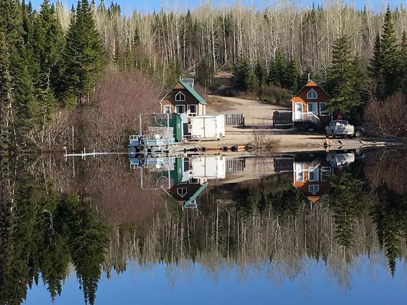 View of two cabins by the lake with a dock and a boat in front.
