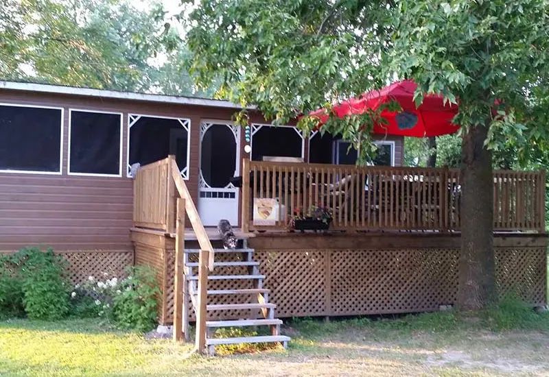 Le chalet Kakawi dispose d'une grande galerie en bois équipée d'un parasol rouge et d'un barbecue.