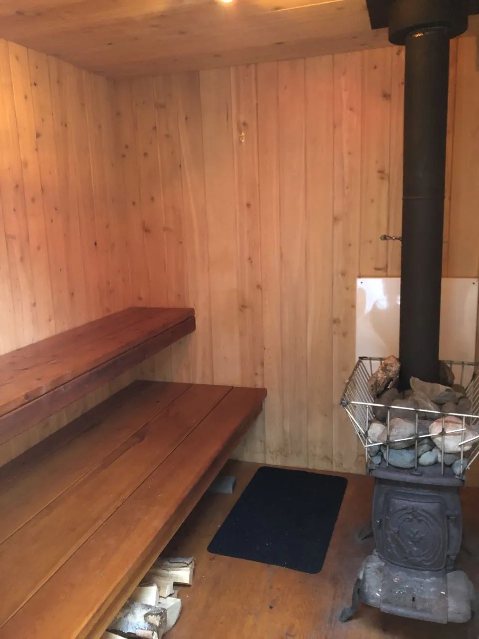 Un sauna rustique en bois avec des bancs intégrés et un poêle à pierres.