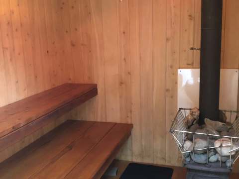 Un sauna rustique en bois avec des bancs intégrés et un poêle à pierres.