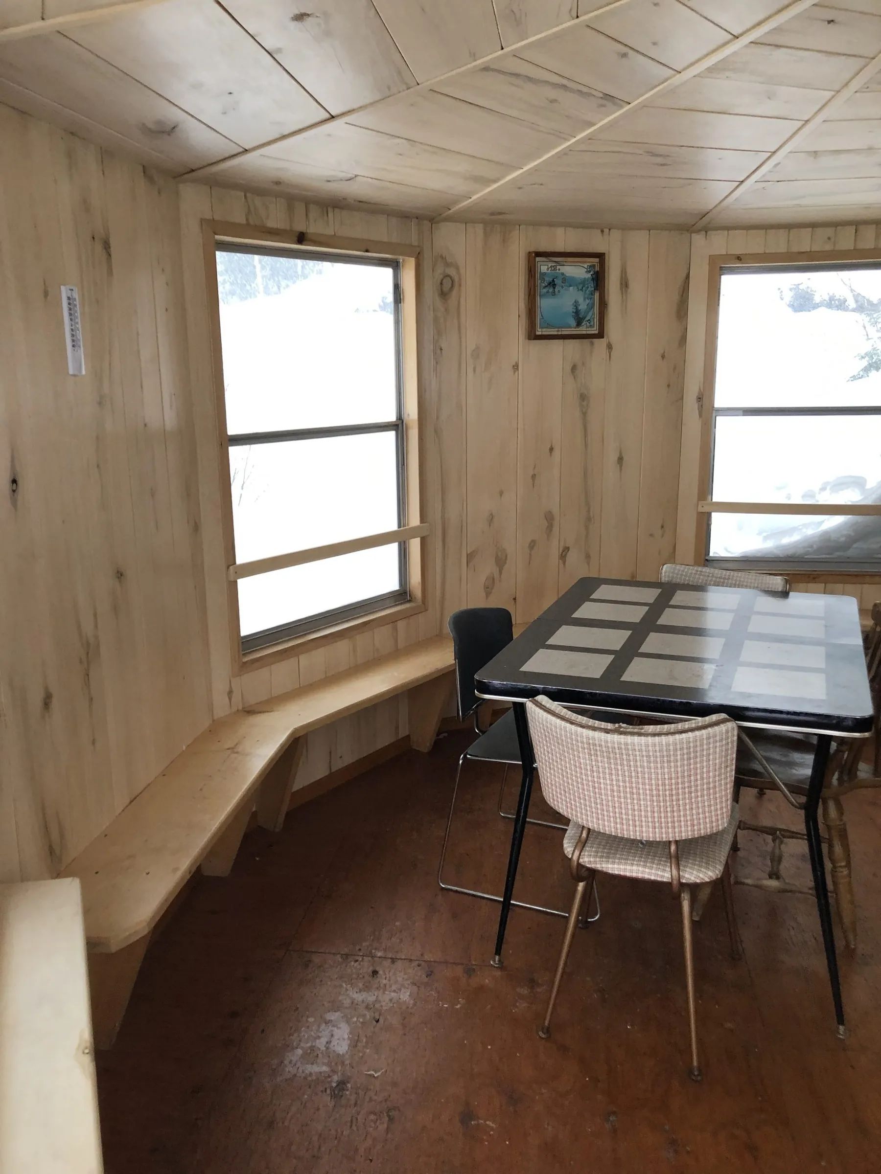 Coin repas rustique en bois avec table, chaises et banc intégré devant la fenêtre.