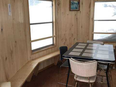 Coin repas rustique en bois avec table, chaises et banc intégré devant la fenêtre.