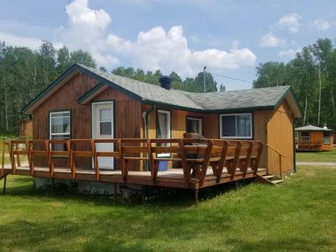 Exterior view of a wooden cabin with a deck and barbecue, located in nature.