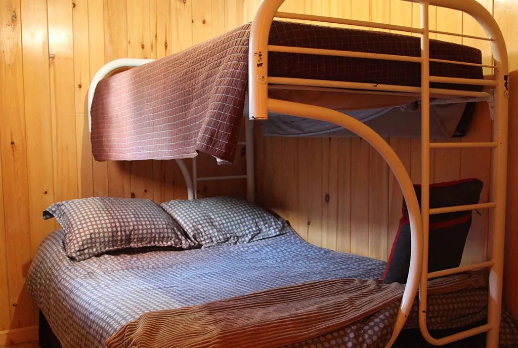 A bedroom with a bunk bed and wooden walls inside the cottage.
