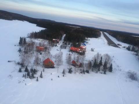 Vue aérienne des chalets et de la piste d'atterrissage sur le site de la pourvoirie en hiver.