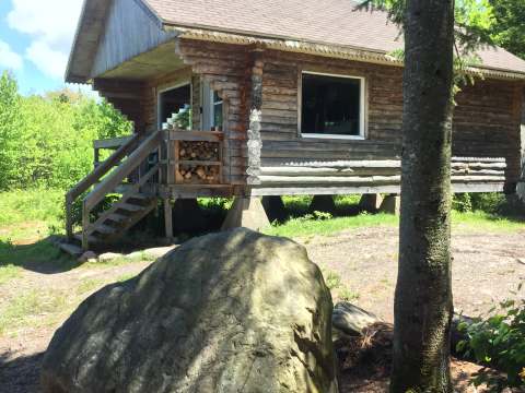 Vue latérale du chalet en bois avec ses escaliers et un grand rocher à proximité.