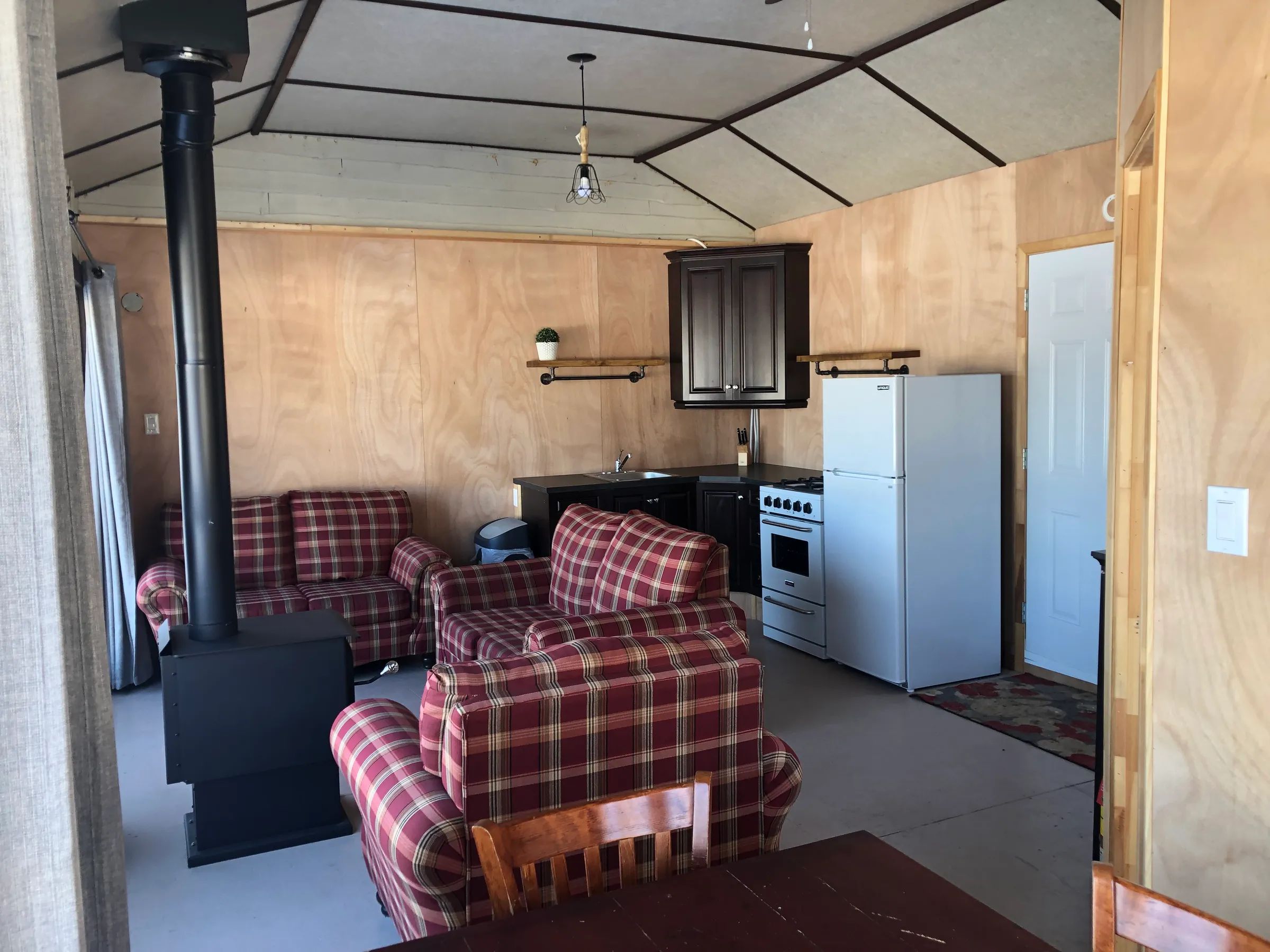 Espace de vie chaleureux comprenant un salon, une cuisinette équipée et un poêle à bois.
