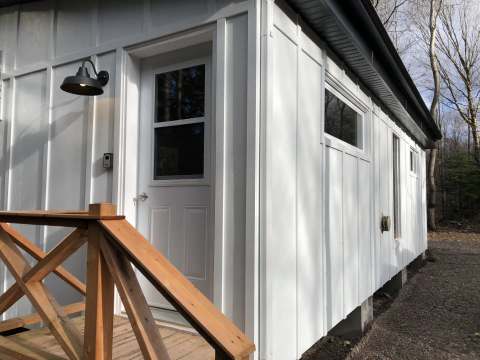 Vue latérale de l'entrée du chalet 7B avec son revêtement blanc et sa rampe en bois.