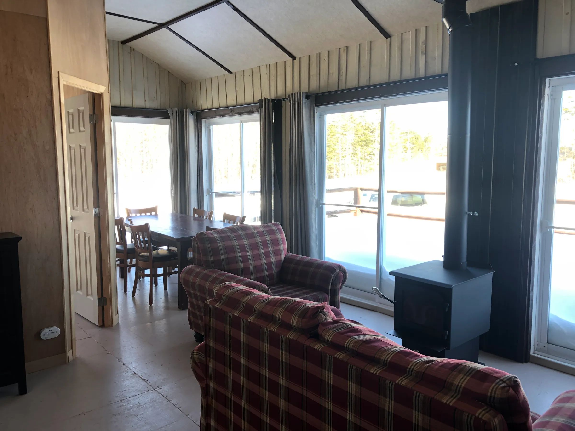 Le salon et la salle à manger du chalet avec poêle à bois et vue sur l'extérieur enneigé.