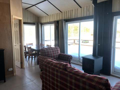 Le salon et la salle à manger du chalet avec poêle à bois et vue sur l'extérieur enneigé.