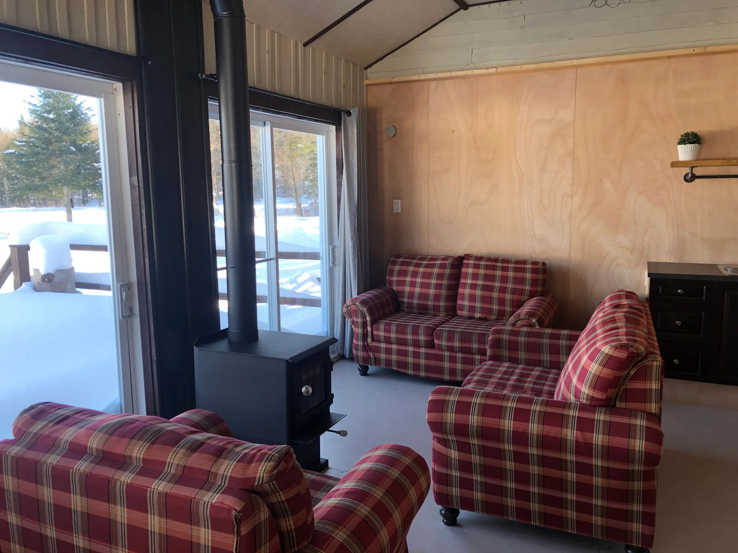 Le salon du chalet comprend des fauteuils confortables et un poêle à bois près de la porte-fenêtre.