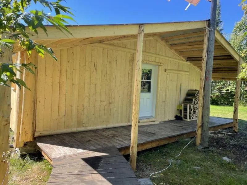 Vue latérale du chalet le Lynx avec sa galerie en bois et son accès extérieur.